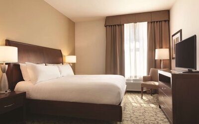 Guest room with king bed, TV, armchair, and window with blackout curtains at Hilton Garden Inn Boston Logan Airport.