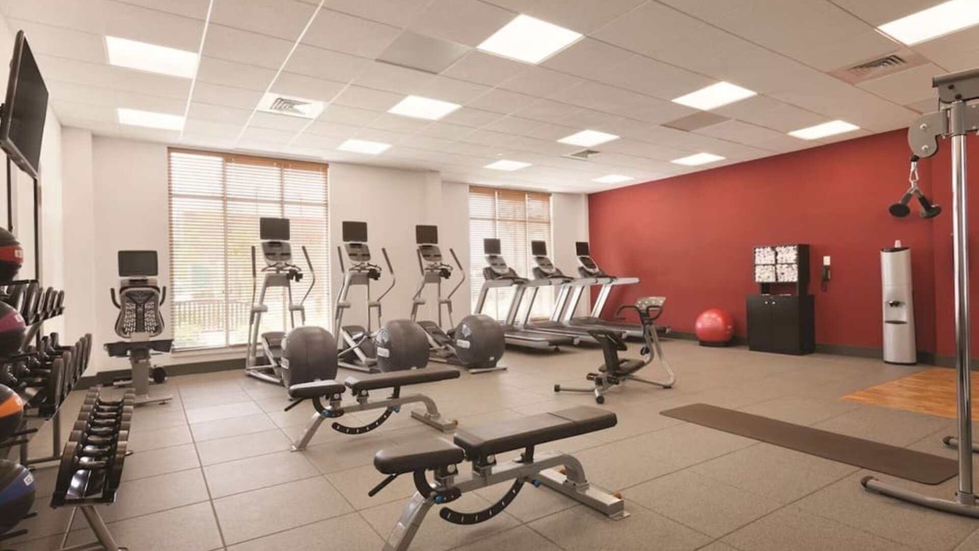 Fitness center with treadmills, weights, exercise benches, and large windows at Hilton Garden Inn Boston Logan Airport.