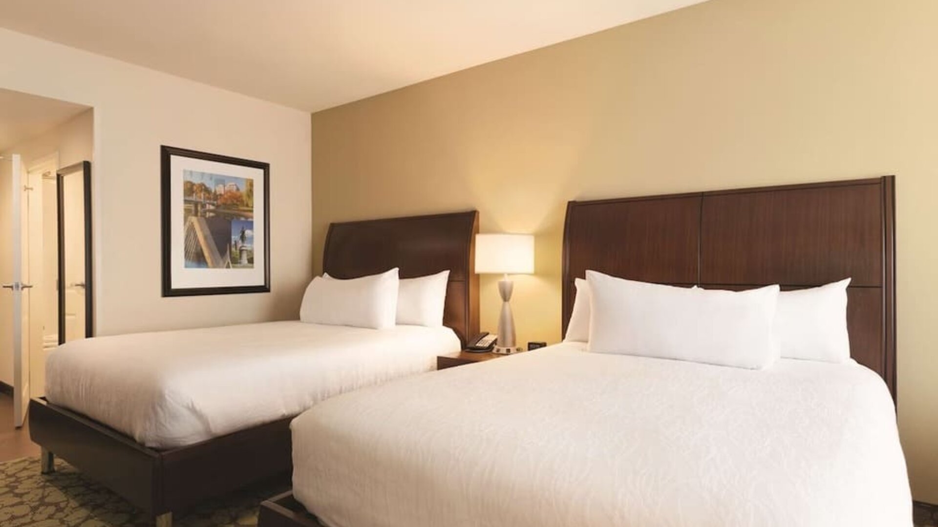 Room with two queen beds, bedside lighting, and framed wall art at Hilton Garden Inn Boston Logan Airport.