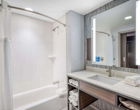 Modern bathroom with illuminated mirror, bathtub shower combo, and marble-style vanity at Hilton Garden Inn Boston Logan Airport.