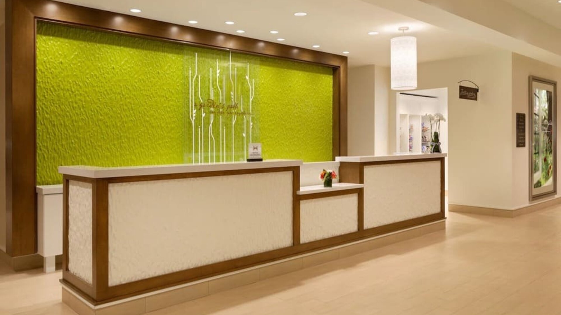 Hotel reception desk with illuminated green accent wall and modern lobby lighting at Hilton Garden Inn Boston Logan Airport.