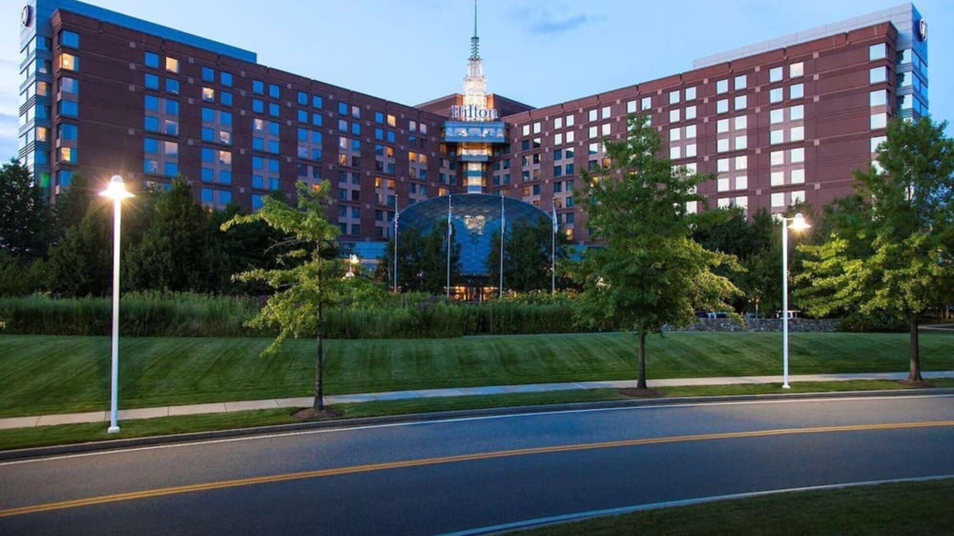 Evening exterior view of Hilton Boston Logan Airport surrounded by landscaped grounds and roadway lighting.