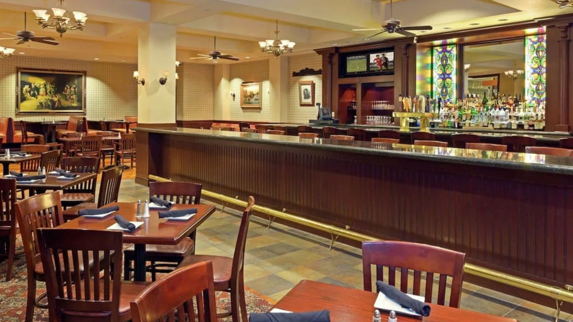 Restaurant and bar area with wooden tables, upholstered seating, and stained glass accents at Hilton Boston Logan Airport.