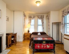 Spacious guest room with double bed, wooden desk, decorative chest, and hardwood floors at The Farrington Inn.