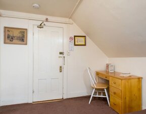 Compact workspace with wooden desk, chair, and sloped ceiling beside entry door at The Farrington Inn.