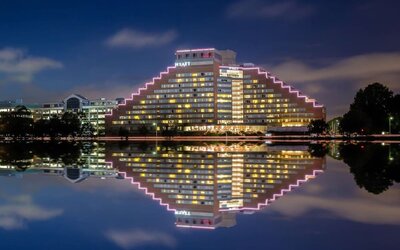 Exterior nighttime view of Hyatt Regency Boston/Cambridge with illuminated pyramid-style architecture reflected on the riverfront.