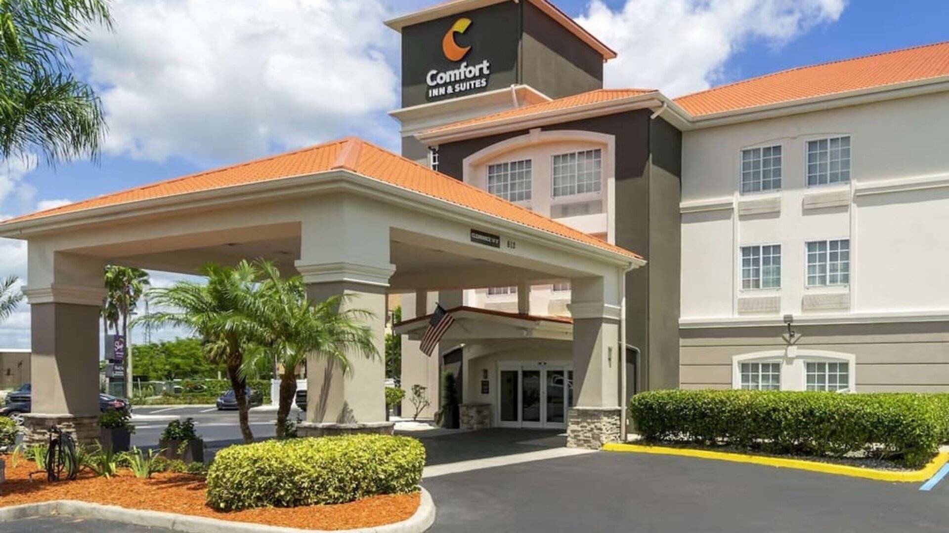 Exterior daytime view of Comfort Inn & Suites Port Charlotte-Punta Gorda with tropical landscaping and covered driveway entrance.