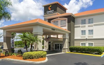 Exterior daytime view of Comfort Inn & Suites Port Charlotte-Punta Gorda with tropical landscaping and covered driveway entrance.