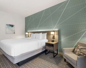 Stylish king guest room with accent wall, plush bedding, and comfortable armchair at Comfort Inn & Suites Port Charlotte-Punta Gorda.