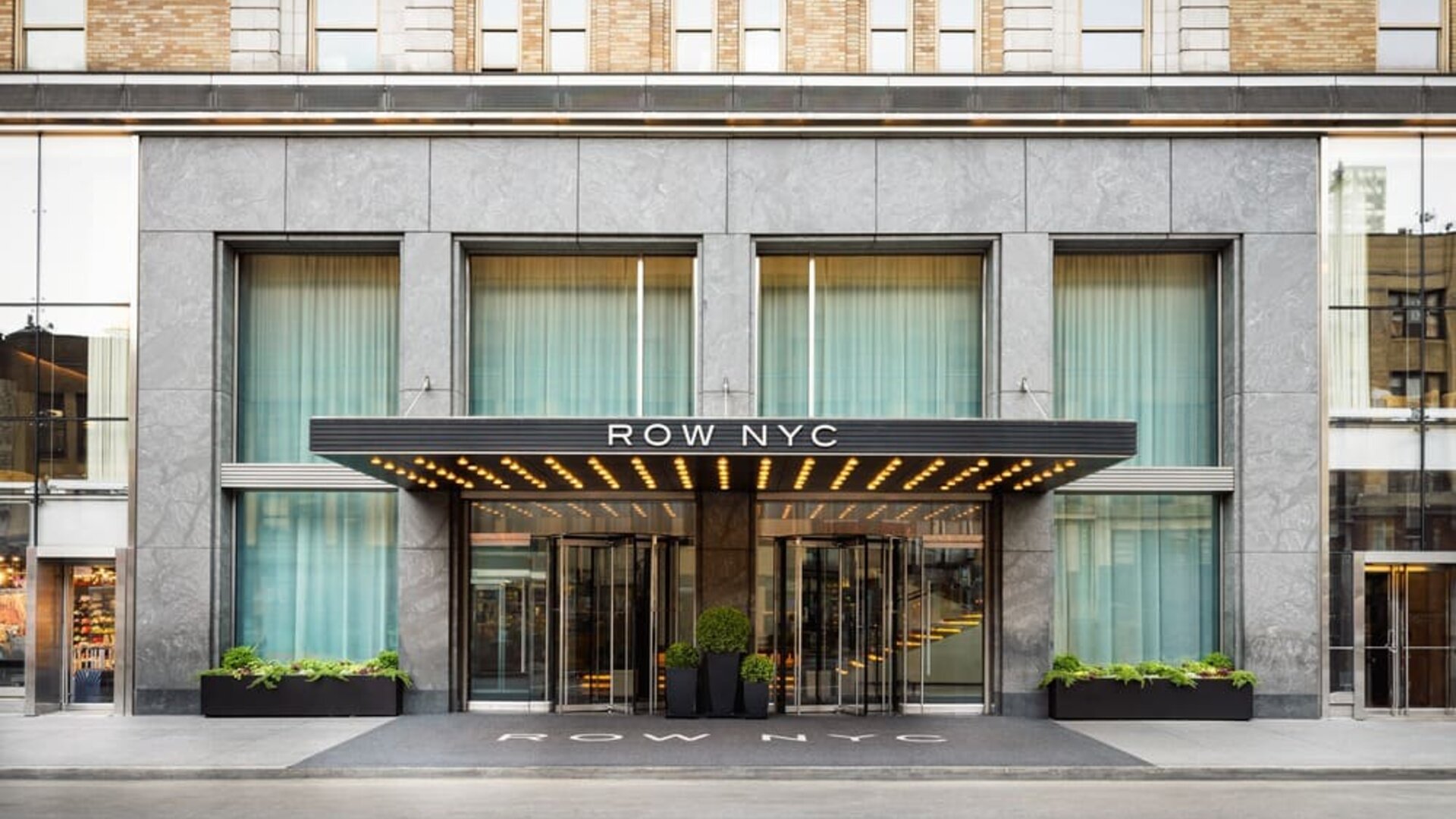 Main entrance façade of Row NYC featuring sleek urban architecture and illuminated signage in Midtown Manhattan.