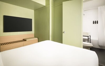 Modern standard guest room with minimalist décor, wall-mounted television, and sleek bathroom access at Row NYC.