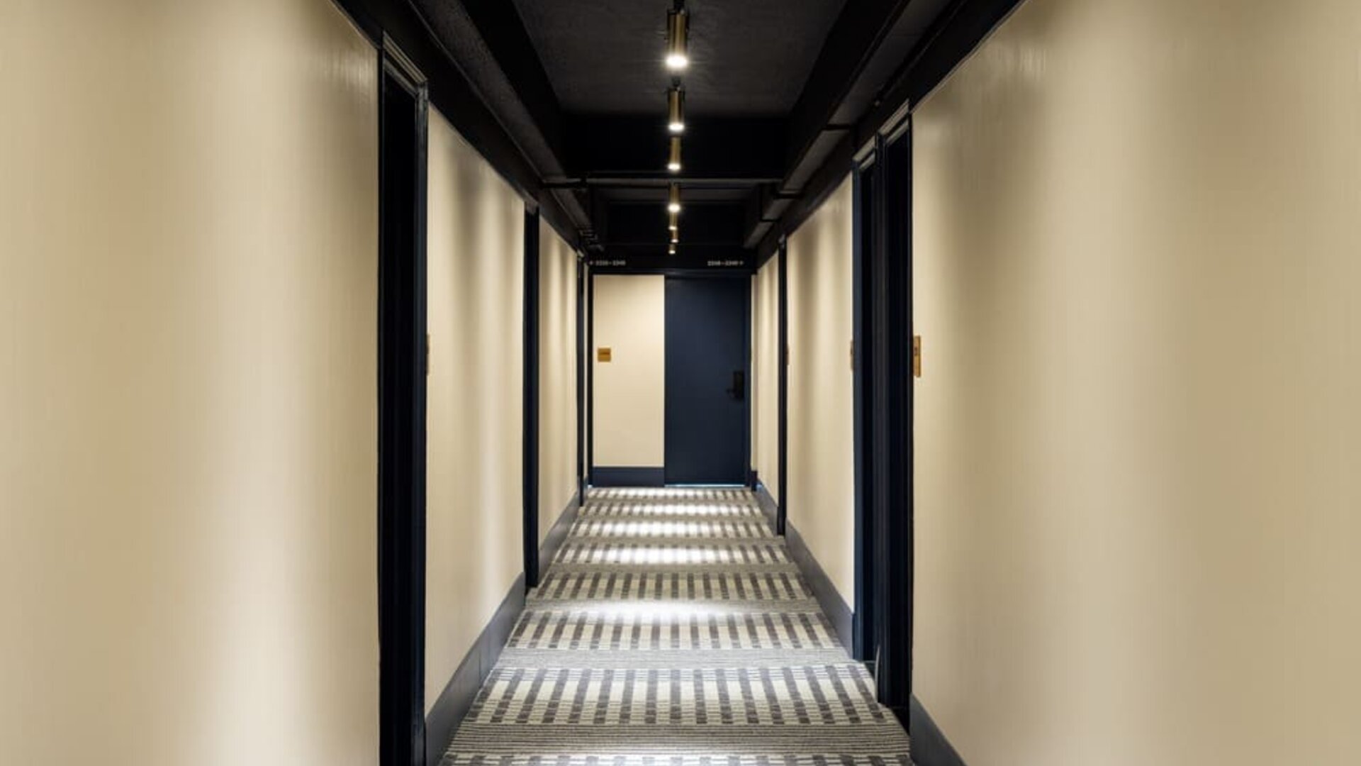 Stylish hotel hallway with patterned carpeting, ambient lighting, and modern guest room entrances at Row NYC.