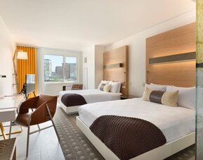 Bright double guest room with two beds, modern furnishings, and large windows offering city views at The Envoy Hotel, Autograph Collection.