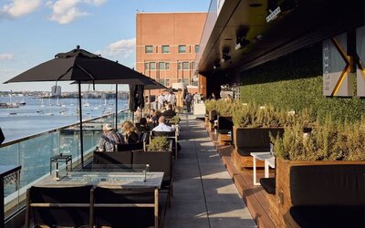 Rooftop outdoor dining terrace overlooking Boston Harbor with lounge seating and scenic waterfront views at The Envoy Hotel, Autograph Collection.