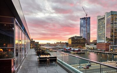 Panoramic rooftop terrace view featuring Boston skyline and waterfront scenery at sunset from The Envoy Hotel, Autograph Collection.