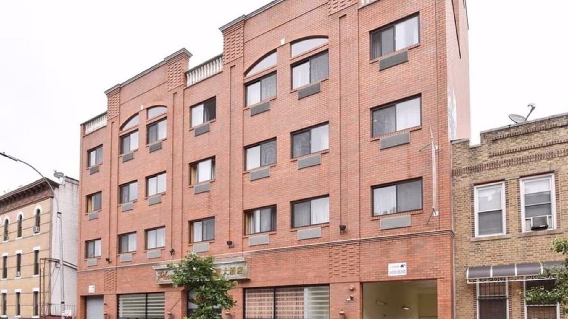 Wide exterior shot of Phoenix Hotel Brooklyn Sunset Park showcasing the multi-story brick building with on-site parking access.