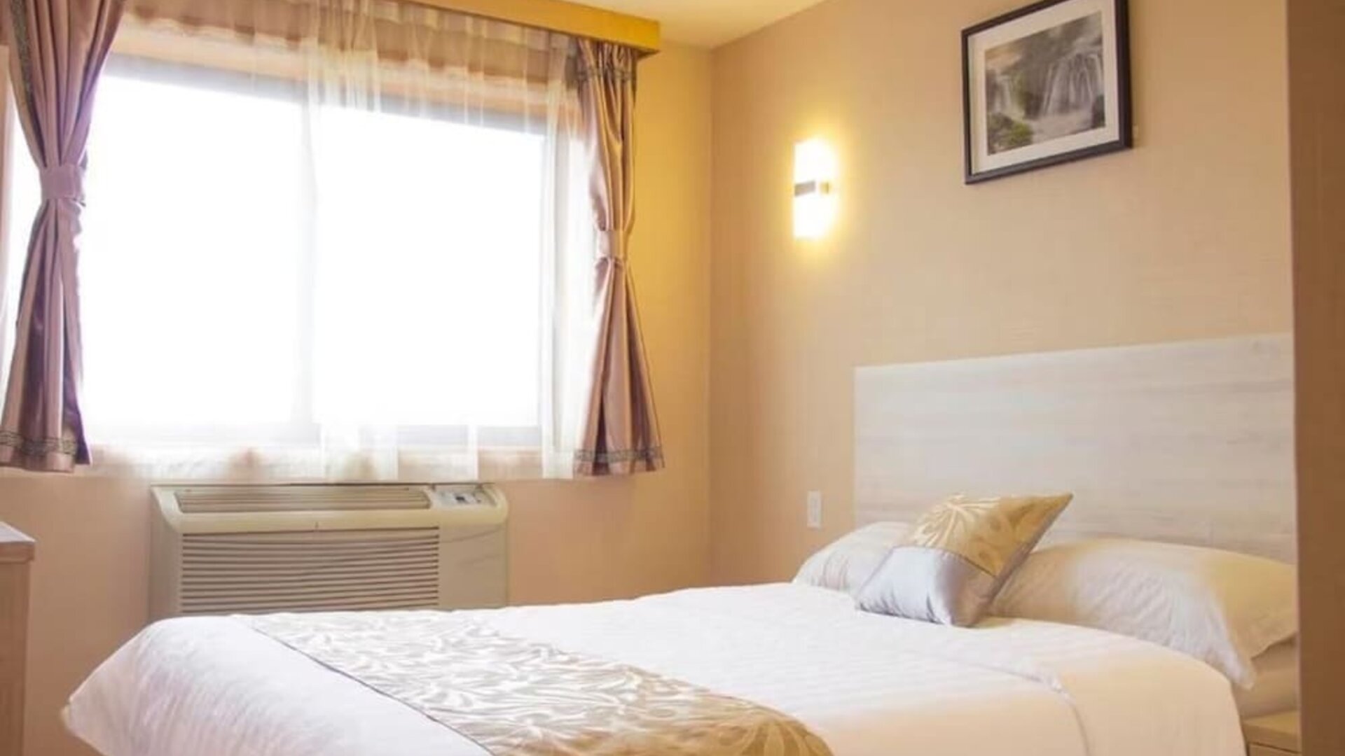 Bright standard guest room with soft neutral décor, natural lighting, and comfortable queen bed at Phoenix Hotel Brooklyn Sunset Park.