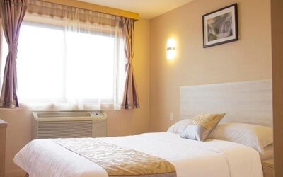 Bright standard guest room with soft neutral décor, natural lighting, and comfortable queen bed at Phoenix Hotel Brooklyn Sunset Park.