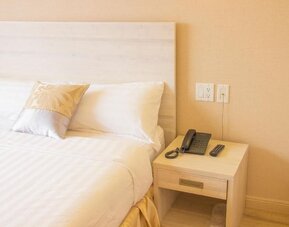 Close-up of a neatly styled guest bed and bedside table with in-room telephone amenities at Phoenix Hotel Brooklyn Sunset Park.
