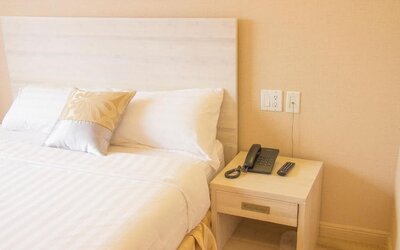 Close-up of a neatly styled guest bed and bedside table with in-room telephone amenities at Phoenix Hotel Brooklyn Sunset Park.