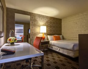 Contemporary guest room at The Garland featuring a comfortable bed, dedicated workspace, warm lighting, and modern mid-century inspired décor.