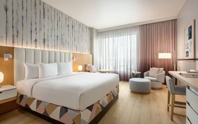 Guest room with a king-size bed, seating area, work desk, and floor-to-ceiling windows offering a bright and relaxing environment.