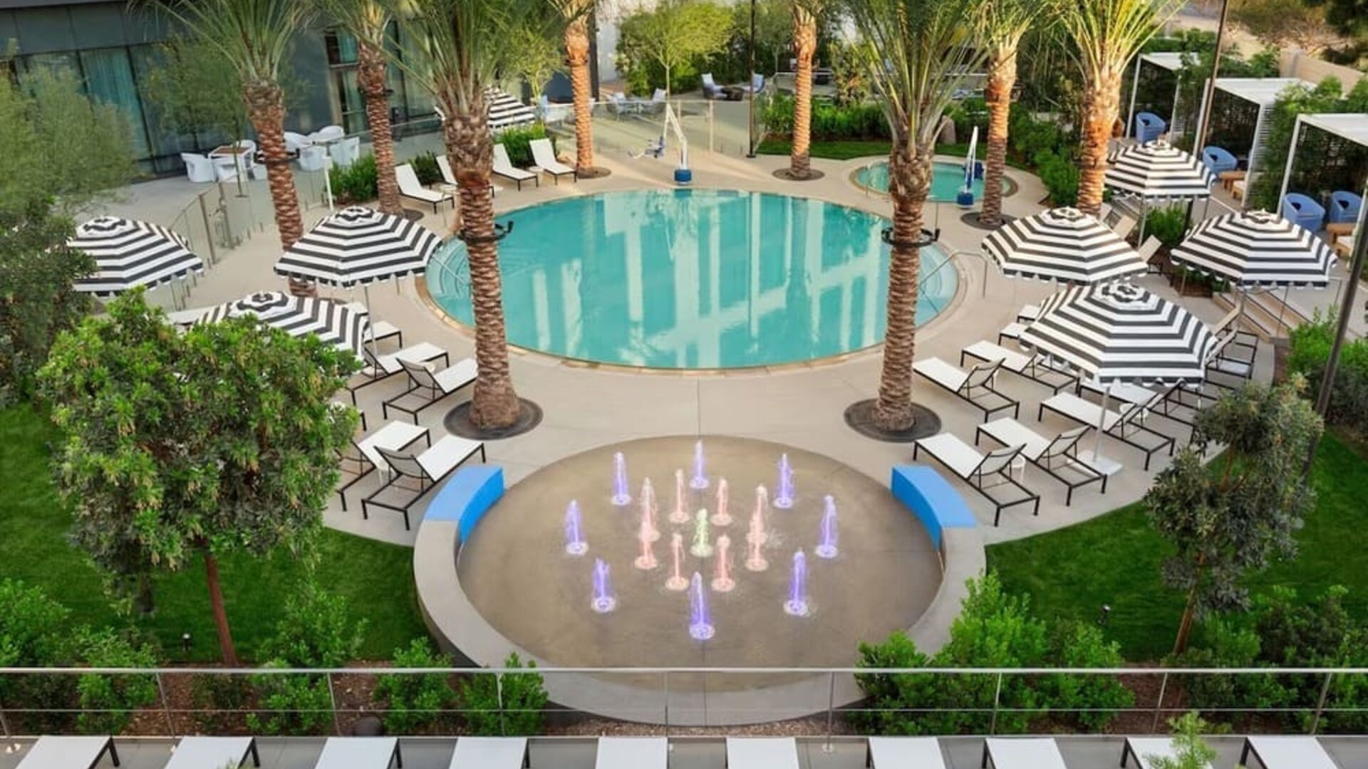 Elevated view of the hotel's outdoor pool complex featuring palm-lined surroundings, lounge areas, and decorative water features.