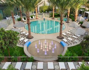 Elevated view of the hotel's outdoor pool complex featuring palm-lined surroundings, lounge areas, and decorative water features.
