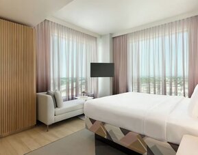 Bright guest room with a king-size bed, floor-to-ceiling windows, comfortable seating area, and panoramic views of the surrounding Anaheim area.