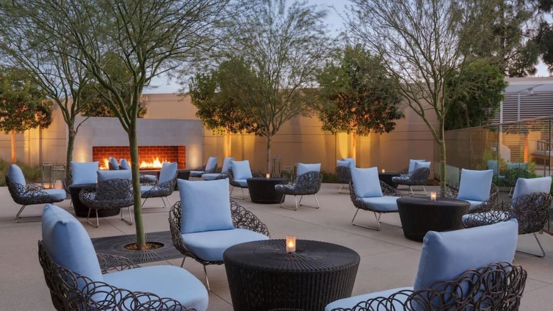 Outdoor courtyard lounge area offering comfortable woven seating, cocktail tables, landscaped surroundings, and a fireplace creating a relaxing social atmosphere.