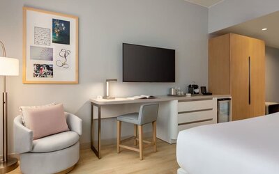 In-room workspace and entertainment area featuring a large flat-screen television, desk, seating, and convenient storage amenities.