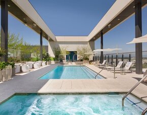 Rooftop pool deck featuring a swimming pool, spa area, sun loungers, shaded seating, and elevated views of the surrounding cityscape.