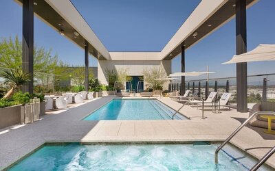Rooftop pool deck featuring a swimming pool, spa area, sun loungers, shaded seating, and elevated views of the surrounding cityscape.