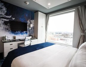 Contemporary king guest room with floor-to-ceiling windows, city views, a dedicated workspace, wall-mounted television, and modern nature-inspired décor.