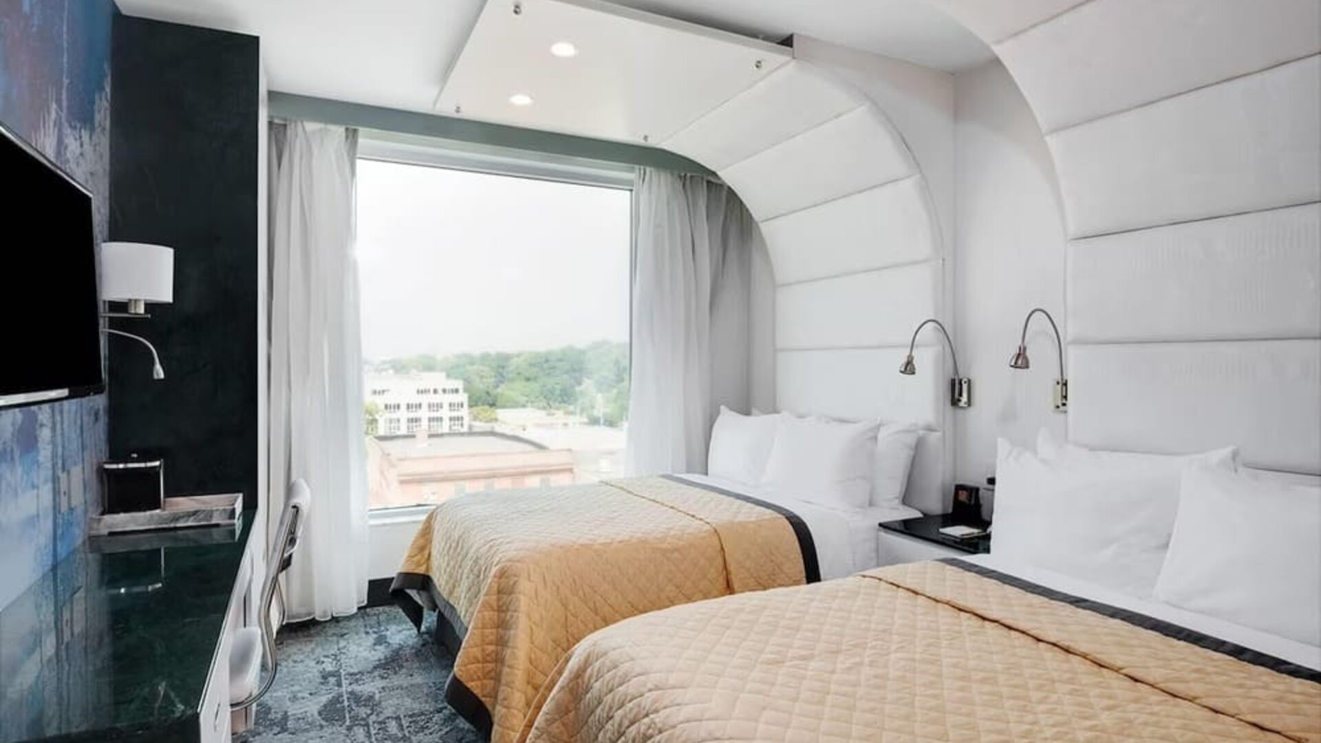 Double-queen guest room featuring two beds, large windows, reading lights, modern furnishings, and a comfortable layout suitable for families or groups.