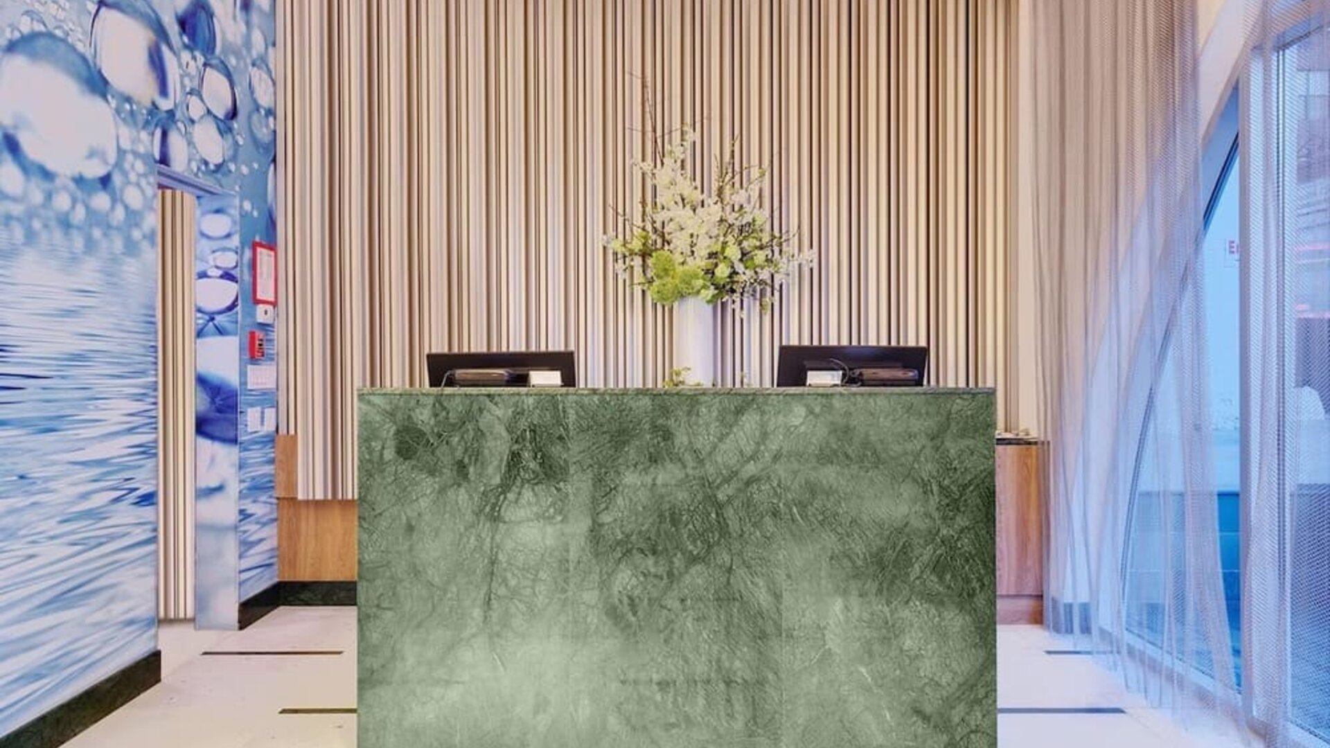 Modern reception area featuring a marble-front front desk, elegant floral arrangements, high ceilings, and a sophisticated lobby design.
