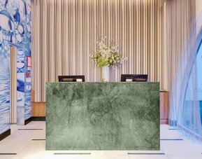 Modern reception area featuring a marble-front front desk, elegant floral arrangements, high ceilings, and a sophisticated lobby design.