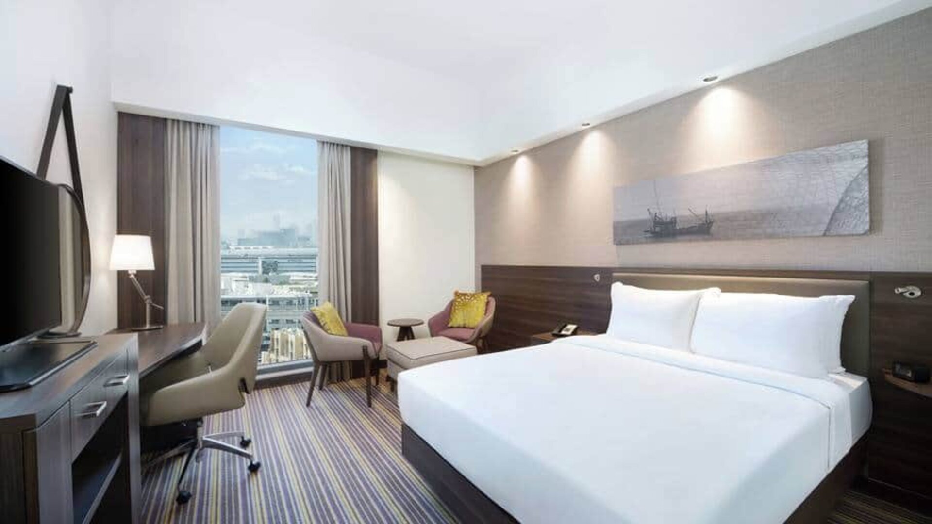 Spacious room with queen bed, desk and chair area at the Hampton Dubai Airport