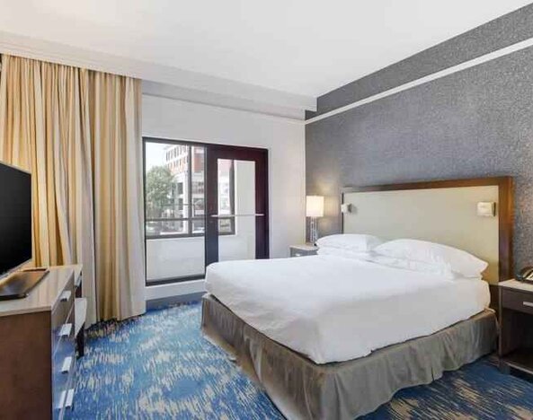 King size bed, large window and TV screen in a king room at the Embassy Suites by Hilton Alexandria-Old Town.