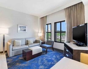 Spacious living room with desk, sofa, TV screen and windows at the Embassy Suites by Hilton Alexandria-Old Town.
