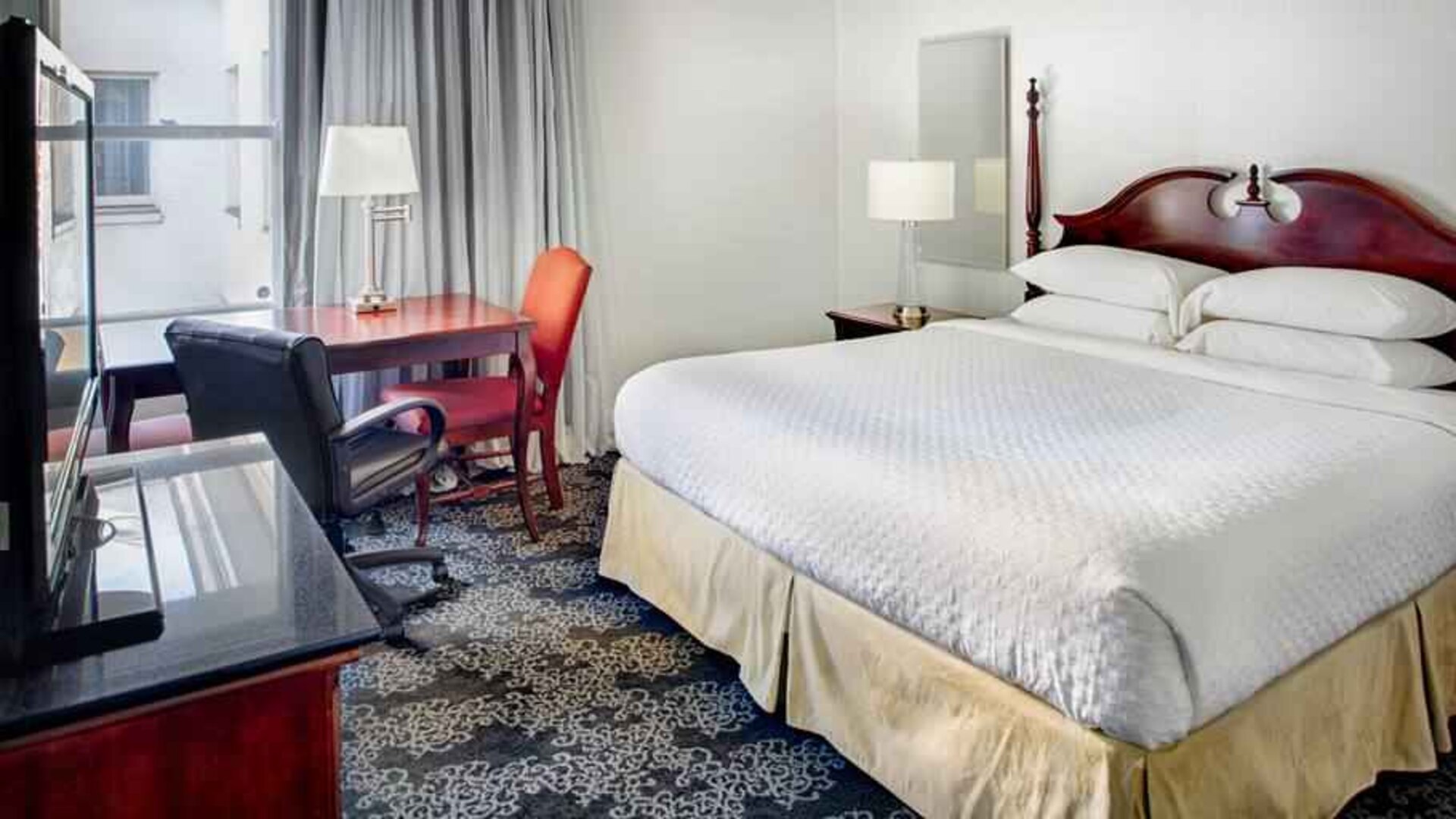 King size bed, desk and TV screen in a hotel room at the Embassy Suites by Hilton Portland-Downtown.