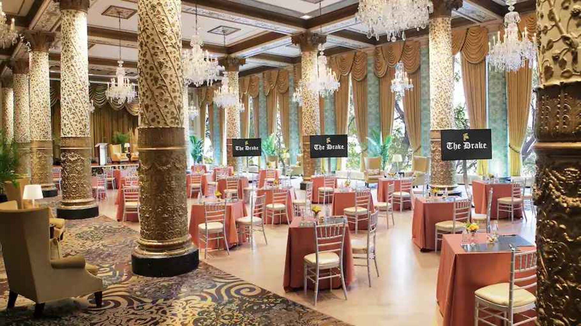 Elegant event room with big windows, lovely chandeliers and intricate pillars at The Drake.