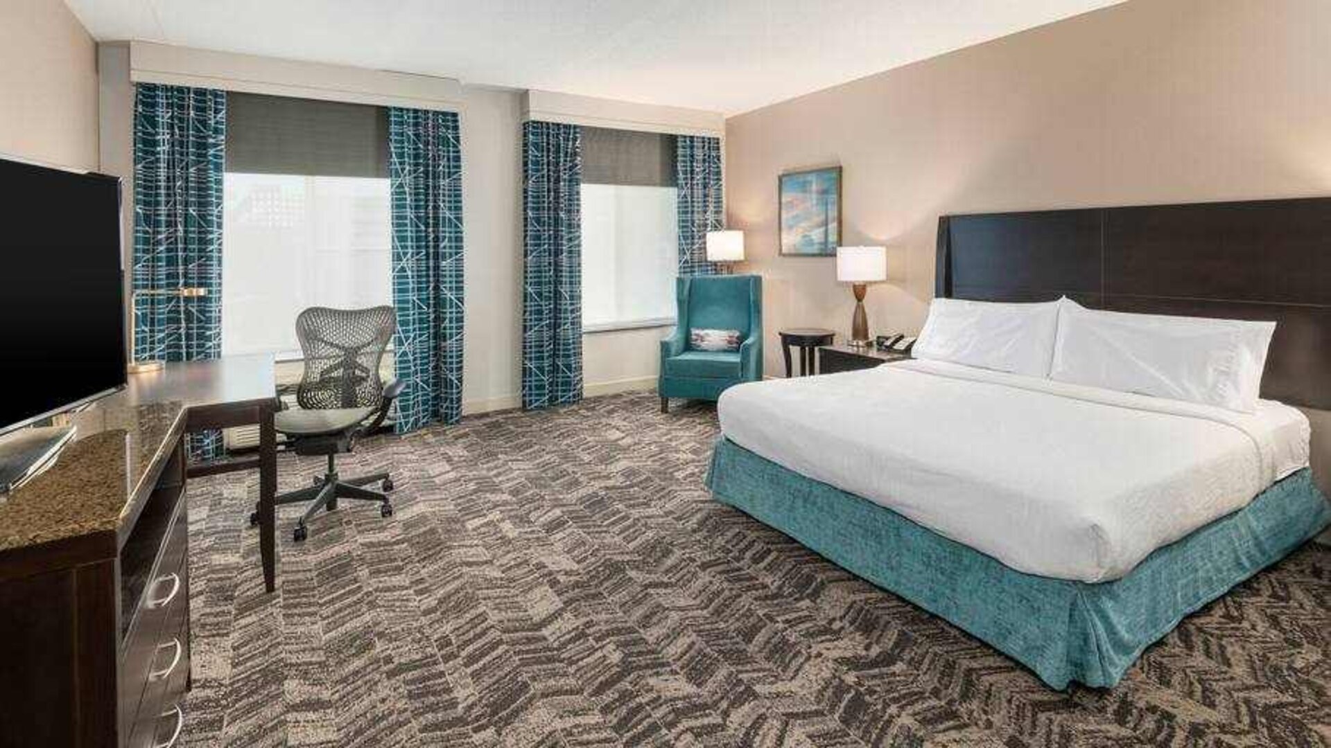 King size bed, sofa and desk in a hotel room at the Hilton Garden Inn Silver Spring White Oak.