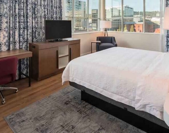 Queen size bed and working station in a hotel room at the Hampton Inn & Suites by Hilton Portland-Pearl District.