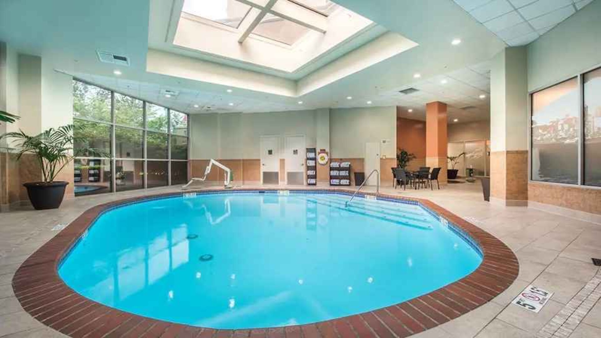 Bright-lit indoor pool with sun roof and comfortable seating area at Embassy Suites by Hilton Seattle Tacoma International Airport.