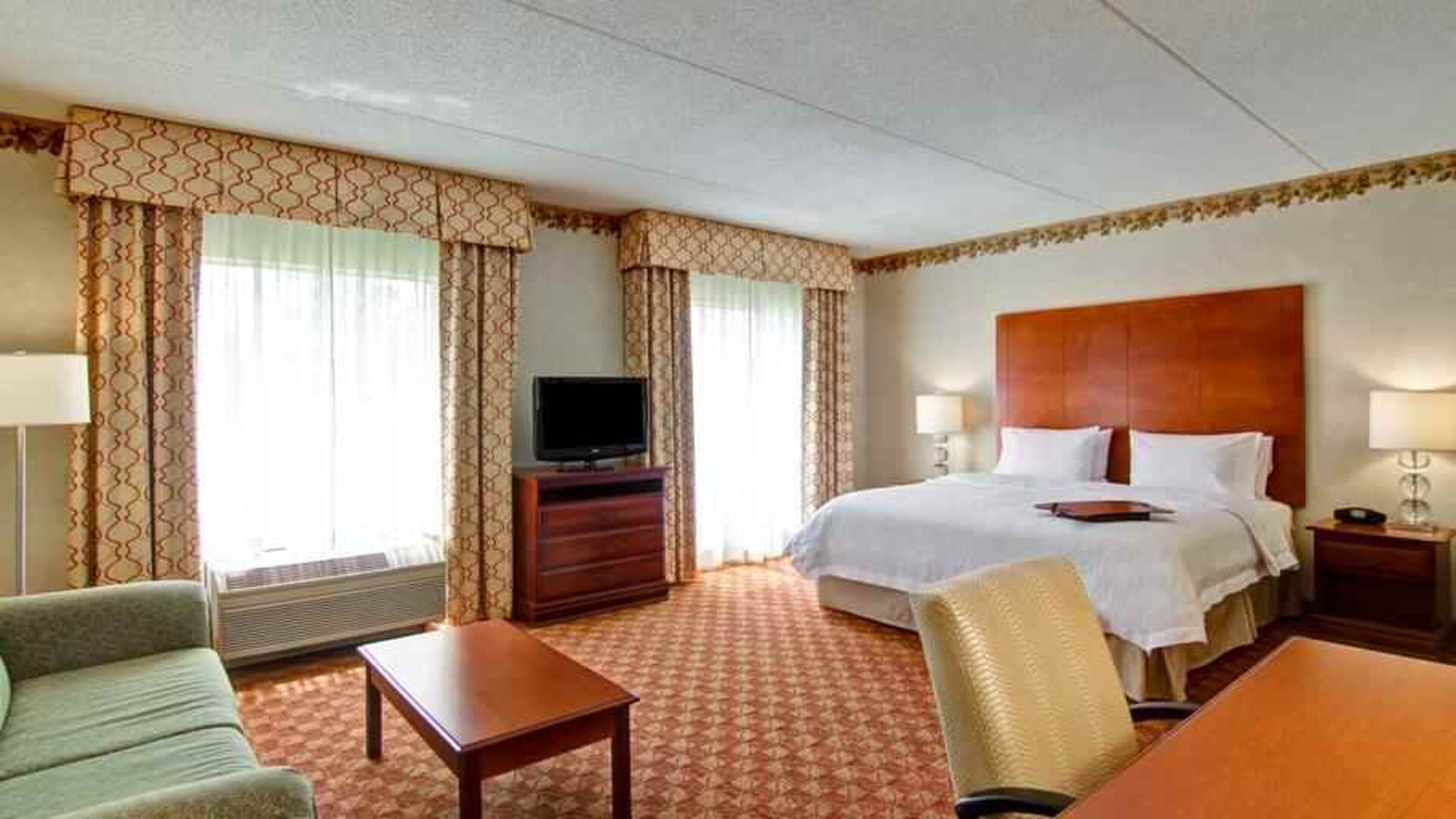 Spacious guestroom with king size bed, sofa and TV screen at the Hampton Inn & Suites Leesburg.