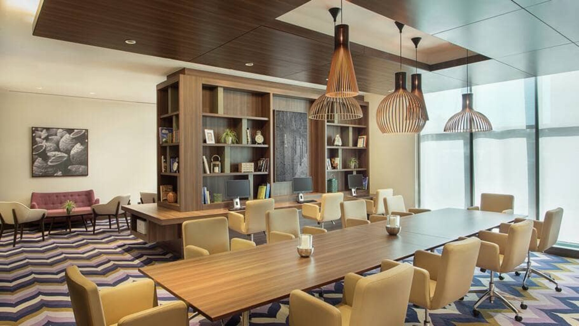 Bronze eclectic lighting hangs over long wooden table lined with floor to ceiling bookshelves.