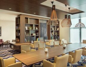 Bronze eclectic lighting hangs over long wooden table lined with floor to ceiling bookshelves.