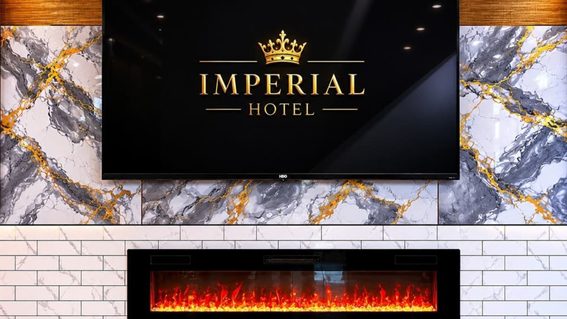 Elegant lobby feature wall at Imperial Hotel showcasing the hotel's branding above a contemporary fireplace, accented with marble-inspired finishes and warm ambient lighting that create a welcoming first impression for guests.