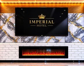 Elegant lobby feature wall at Imperial Hotel showcasing the hotel's branding above a contemporary fireplace, accented with marble-inspired finishes and warm ambient lighting that create a welcoming first impression for guests.